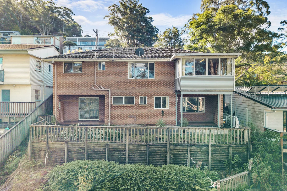 Two storey brick rear facade with a timber fence and an overgrown garden, before