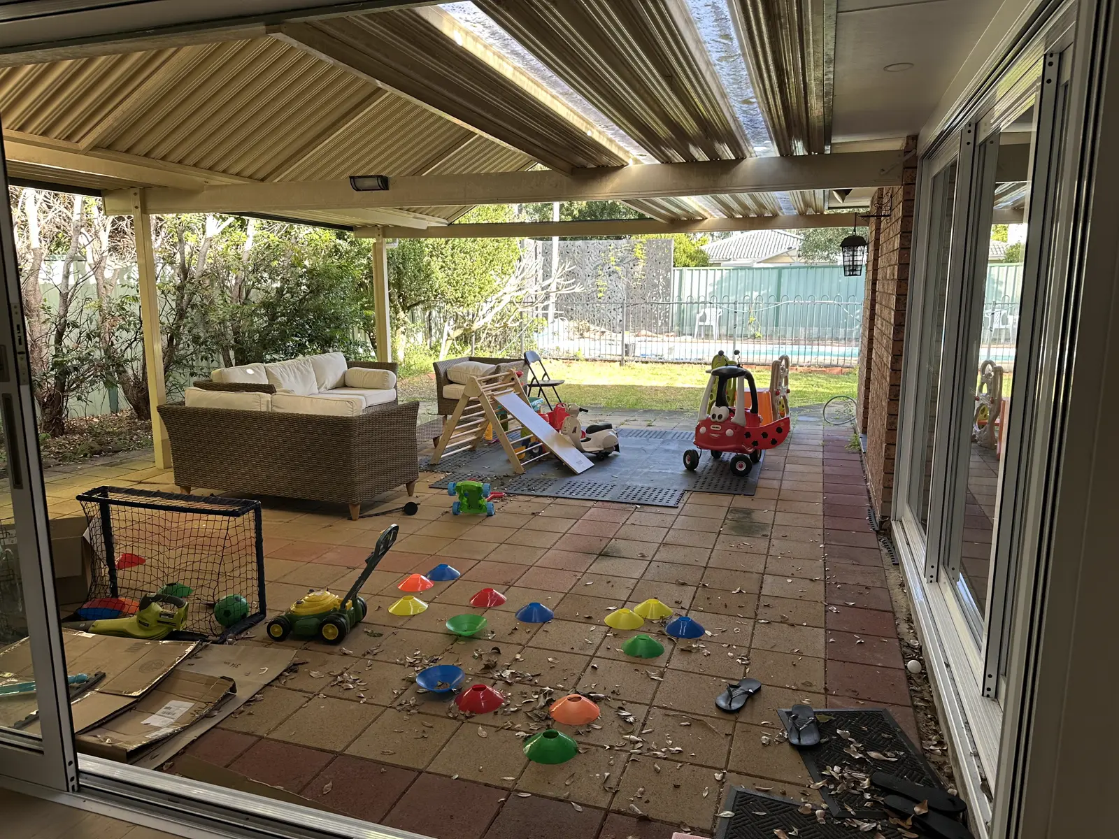 Covered outdoor area with a tiled floor, a cane lounge and a pool beyond, before
