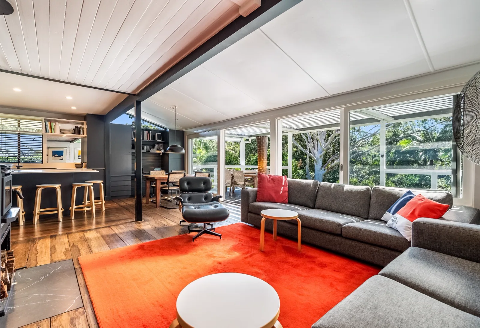 Open plan living room with grey sofas, an orange rug and timber floors, before